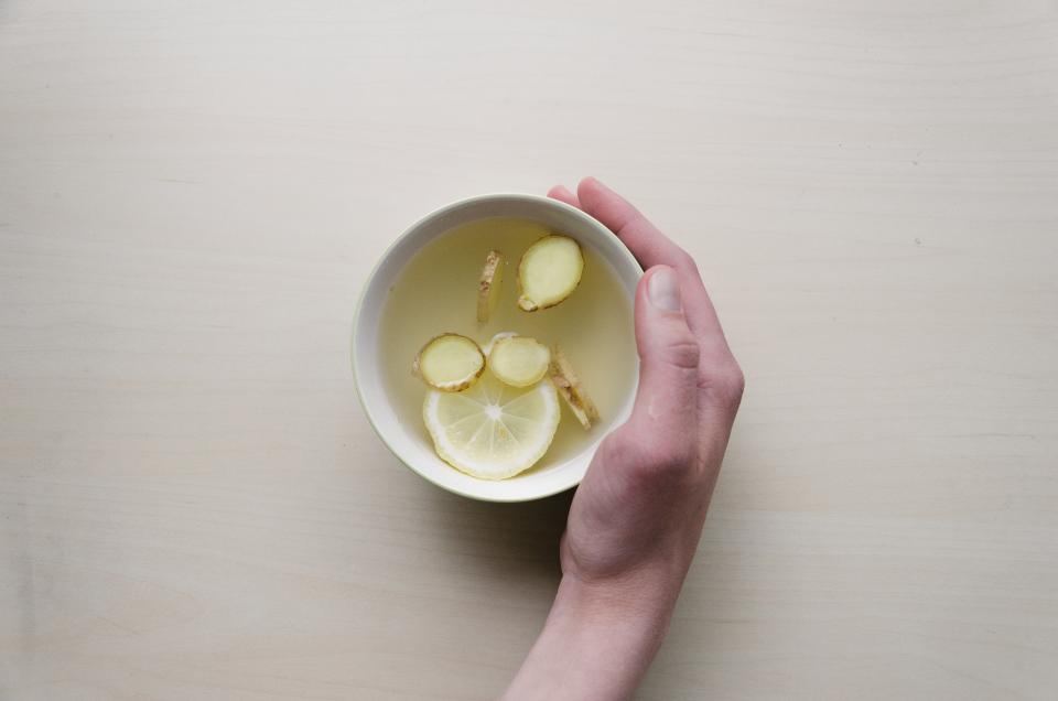A cup of ginger tea held in one hand on a table