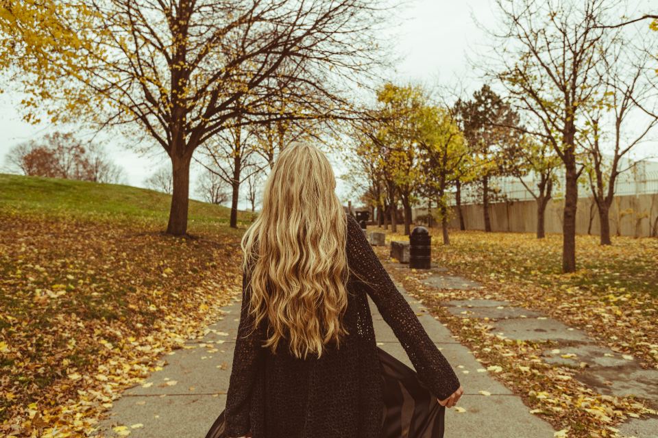 A woman walking on a path covered in autumn leaves